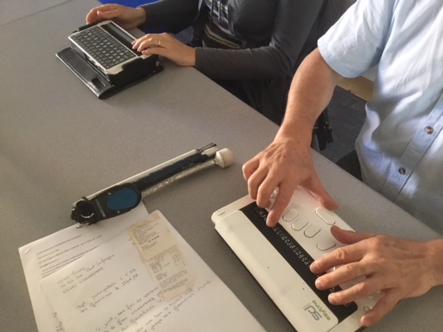 administratrice et administrateur utilisant un ordinateur avec clavier Braille, entre les claviers une canne blanche , pliante et pliée